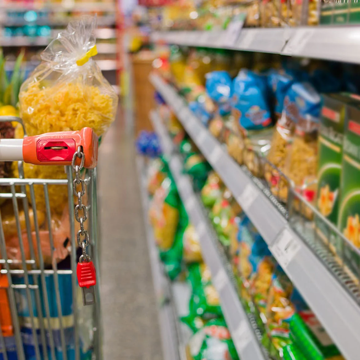 Carro de supermercado junto a una góndola con productos alimenticios