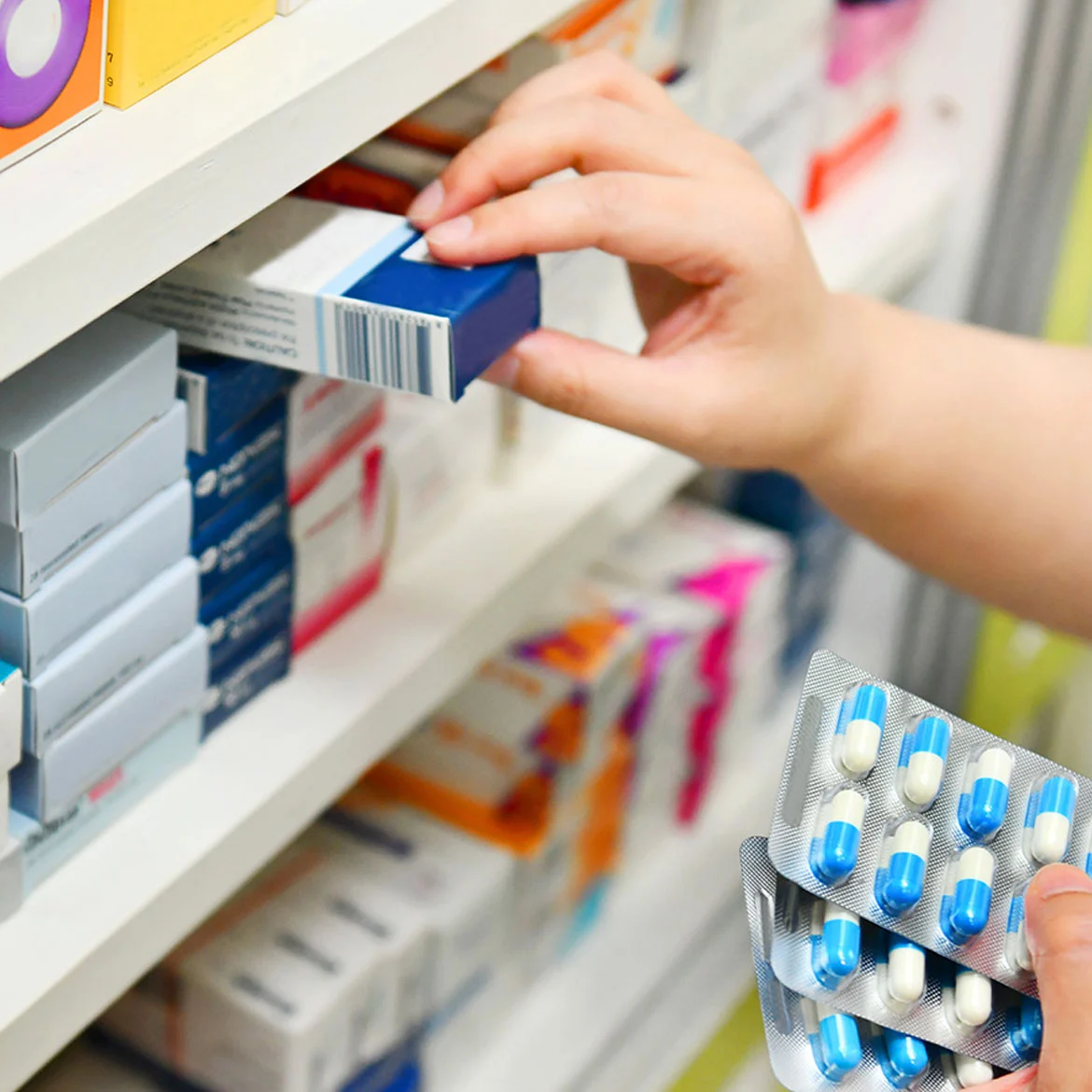 Persona seleccionando un medicamento en una góndola de farmacia