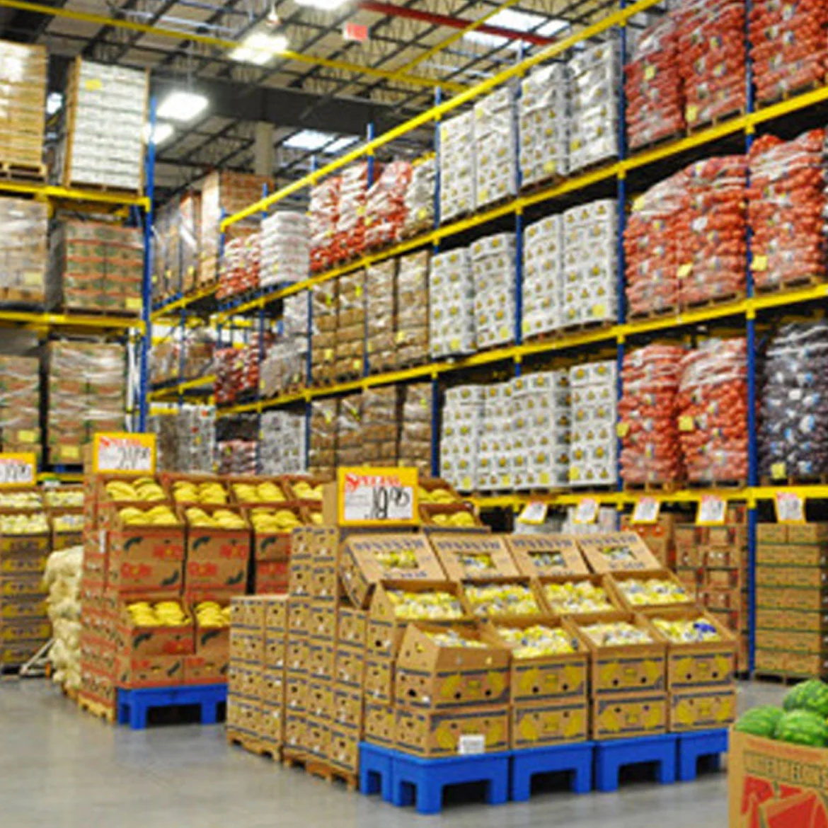 Bodega de mayorista con cajas de frutas y mercadería en pallets
